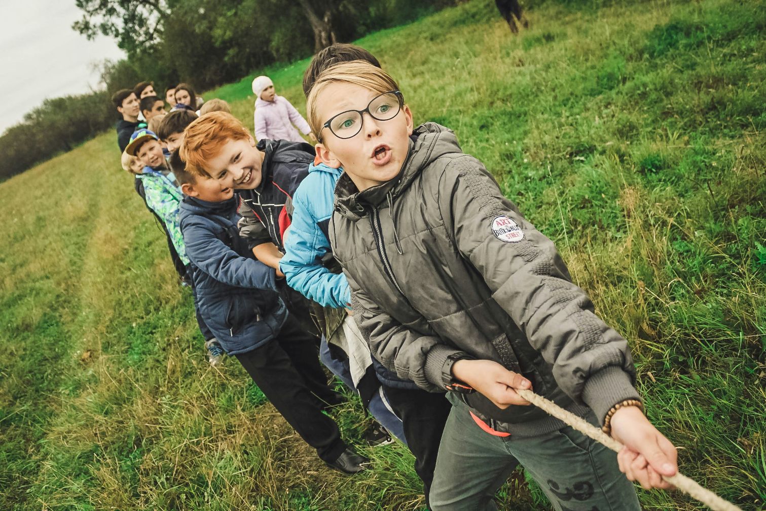 Group of children playing tug of war in a grassy field, building teamwork and friendships during a home‑education day.