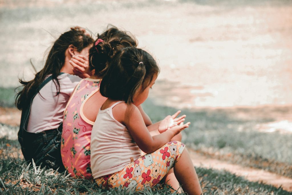 Three children sitting together on the grass outdoors, enjoying a calm moment during a home‑education activity.